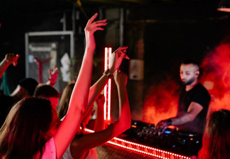 Partygoers with raised hands at a nightclub, DJ mixing music