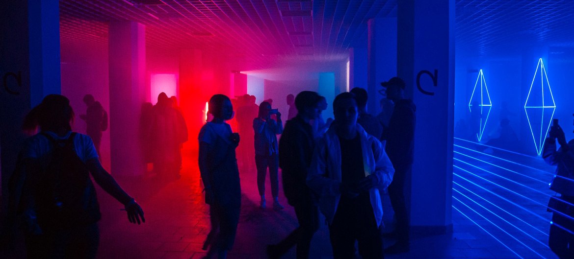 People silhouetted in a neon-lit hallway, vibrant pink and blue lights.