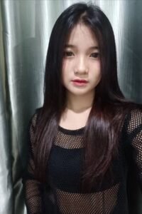 Portrait of a young woman with long dark hair, wearing a black mesh top.