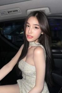 Attractive young woman in a light-colored dress sits in a car.