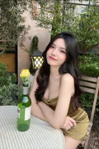Attractive young woman in a gold dress sits at a table outdoors.